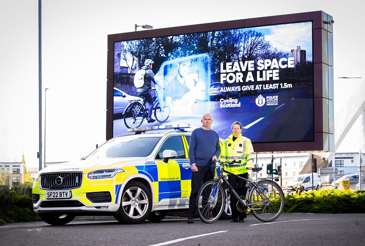 Two people stand in front of a billboard for the Cycling Scotland campaign